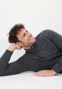 Grauer Reißverschluss-Pullover aus strukturiertem Strickstoff, mit Stehkragen und dezenten Farbdetails. Model liegt lächelnd auf dem Boden.