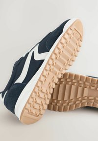 Sneakers met een navy blauwe bovenkant, gemaakt van suède en stoftexturen, witte accenten en een rubberen buitenzool met een gemustreerd profiel.