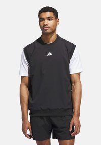 Černý bezrukávový sportovní top s kulatým výstřihem, který má bílé logo. Spárován s černými šortkami, obojí z hladkého materiálu.