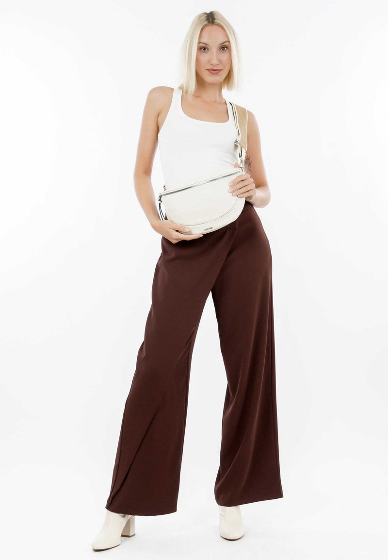 Hvid tanktop kombineret med højtaljede, brede brune bukser. Modellen holder en cremefarvet crossbody taske med lynlås. Hvid baggrund.