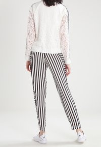 Bílý krajkový top s dlouhým rukávem a jednobarevným zadním dílem, spojený s černobílými pruhovanými zúženými kalhotami a bílými teniskami.