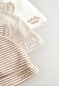 Set van drie katoenen babyhoedjes. Kleuren: crème, beige en bruin met patronen. Kenmerken: geribbelde textuur, schattige berenoortjes en geborduurde accenten.