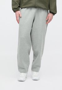 Sive trenirke iz mehke tkanine, z udobnim krojem in elastičnim pasom, kombinirane z belimi supergami na nevtralnem ozadju.