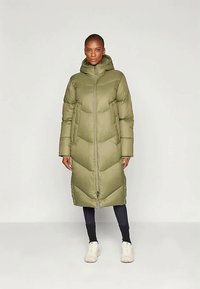 Manteau matelassé vert olive avec capuche, présentant une fermeture éclair à l'avant, des manches longues et un motif en chevrons. Tissu texturé avec un design de longueur intermédiaire.