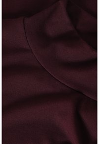 Burgundin kangas, jolla on sileä, hieman kiiltävä pinta ja rento kaulusmuotoilu, jossa on pehmeitä, ribbimuotoja ja lempeää laskeutumista.