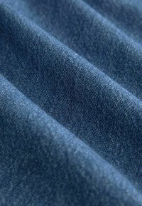 Denim-kangas syvässä sinisessä sävyssä, jossa on sileä rakenne ja hienovaraisia variatioita. Materiaali näyttää klassiselta kudontalta.