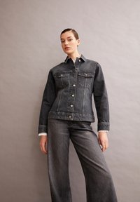 Donkerdenim jacket met een knoopsluiting aan de voorkant, twee borstzakken en een klassieke kraag, gecombineerd met bijpassende wijde jeans.