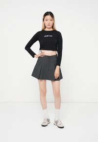 Black cropped long-sleeve top with "Santa Cruz" text, paired with a grey pleated skirt. Worn with white socks and light-colored shoes.