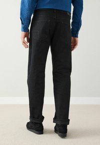 Svarta jeans med rak passform, synliga bakfickor, uppvikta fållar och texturerat tyg, kombinerade med svarta mockaskor.