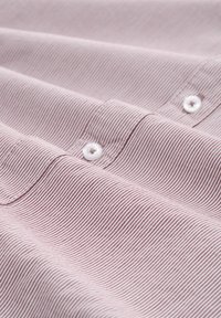 Nahaufnahme eines pink- und weißgestreiften Stoffes mit Knopf- und genähten Nahtdetails auf einem Kleidungsstück.