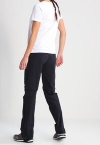 Černé venkovní kalhoty s nastavitelnými manžetami, spárované s bílou košilí s krátkým rukávem. Tkanina vypadá lehce a zároveň odolně.