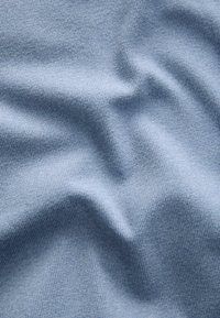 Sininen neulottu kangas, jossa on pehmeä tekstuuri, hienovarainen röyhelökuvio ja hellät poimut.