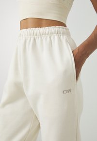 Hvite joggebukser med elastisk midjebånd, med en sidelomme og subtilt brodert logo. Myk stoff med glatt tekstur.