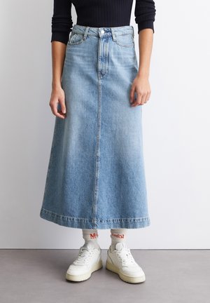 Denim maxi skirt in light blue with a front button closure, two side pockets, and a straight silhouette. Paired with white sneakers and socks.