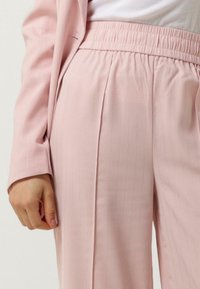 Broek in zachtroze stof met verticale strepen en een elastische tailleband. Het op maat gemaakte ontwerp heeft gestructureerde plooien en een gladde textuur.