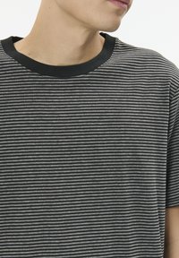 Black and gray striped short-sleeve t-shirt with a black ribbed neckline. Soft fabric with horizontal lines and a relaxed fit.