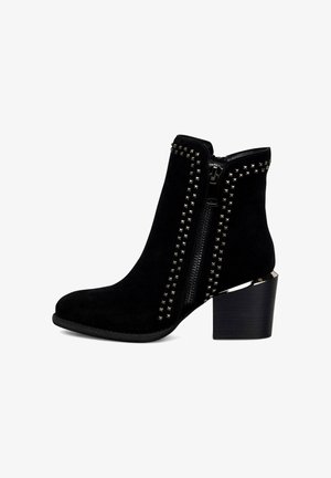 Bottines en daim noir avec des accents en clous argentés le long de la fermeture éclair et des côtés, dotées d'un talon épais noir et d'une surface texturée.