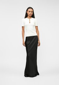 Biała dopasowana bluzka z krótkimi rękawami i dekoracyjnym detalem w postaci guzika, zestawiona z czarną satynową spódnicą do ziemi. Gładka tekstura na całej powierzchni.