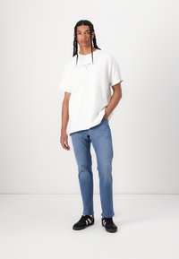 Hvid bomulds t-shirt med blå tekst og afslappet pasform, kombineret med lyseblå jeans og sorte sneakers med hvide striber.