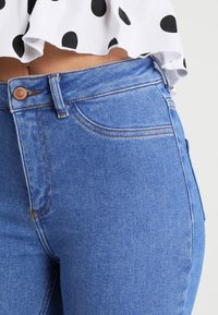 Vaqueros de mezclilla de corte alto en azul claro con un botón de cobre, que cuentan con un bolsillo frontal, una sutil textura de costura y un corte recto.