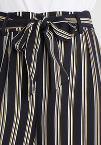 Vysoké, námořnické kalhoty s vertikálními pruhy v žluté a bílé barvě. Má zavazovací pásek vpředu a měkkou, texturovanou tkaninu.