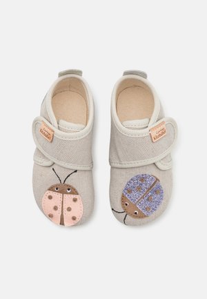 Morbide scarpe beige per bambini con chiusure in velcro, ciascuna decorata con un diverso disegno di coccinella: rosa sulla scarpa sinistra e viola sulla destra.