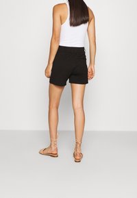 Shorts noirs avec taille élastique, associés à des sandales beige à brides. Tissu lisse, coupe au milieu de la cuisse, et design décontracté.