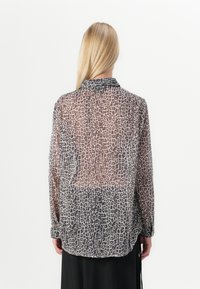 Camisa de manga longa transparente em bege com um padrão de leopardo escuro. Apresenta colarinho e fecho com botões. Textura suave com um corte solto.