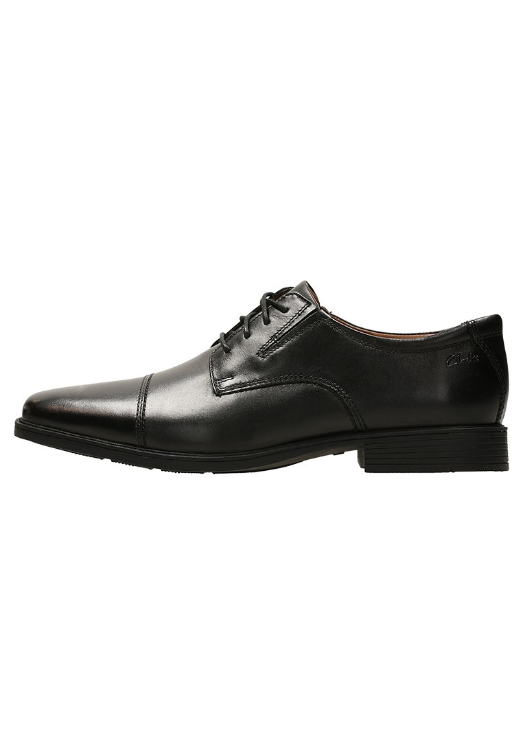 Zapato de vestir de cuero negro con punta afilada, diseño sencillo de cordones, suela plana de goma y detalles de costura mínimos.