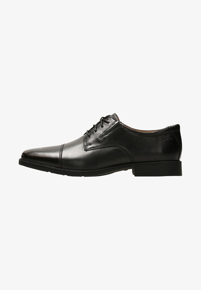 Chaussure habillée en cuir noir avec un bout pointu, un design simple à lacets, une semelle en caoutchouc plate et des détails de surpiqûres minimaux.