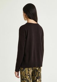 Maglione marrone scuro a maglia con orlo a coste, spalle scese e vestibilità ampia, abbinato a pantaloni con motivo floreale.
