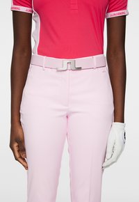 Rosa golfbyxor i lättviktsmaterial, med en metallisk silverfärgad bältes-spänne och en vit golfhandske på höger hand.
