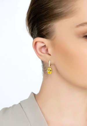 Gold hoop earrings featuring a large yellow gemstone with faceted details, shown against a neutral background and worn on a model.