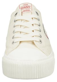 Zapatillas de lona en color crema, con punta redonda, suela de goma blanca y ojales de metal. Presentan un parche con el logotipo en rojo y blanco cerca de la lengüeta.