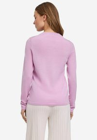 Hellrosa langärmliger Pullover aus weichem Strickstoff, mit Rundhalsausschnitt und gerippten Bündchen. Kombiniert mit strukturierten cremefarbenen weiten Hosen.