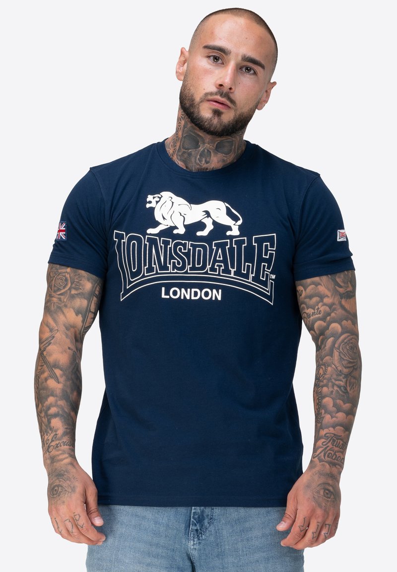Granatowa bawełniana koszulka z krótkim rękawem z białą grafiką lwa i napisem "Lonsdale London", z naszywką z brytyjską flagą na rękawie.