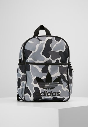 Plecak z czarnym, białym i szarym wzorem kamuflażu, przednia kieszeń na zamek, czarne logo Adidas i czarna górna rączka na jednolitym tle.