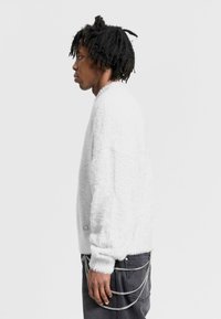 Oversized white fuzzy sweater with long sleeves, textured fabric, and a ribbed cuff. Paired with dark jeans featuring metal chain accents.