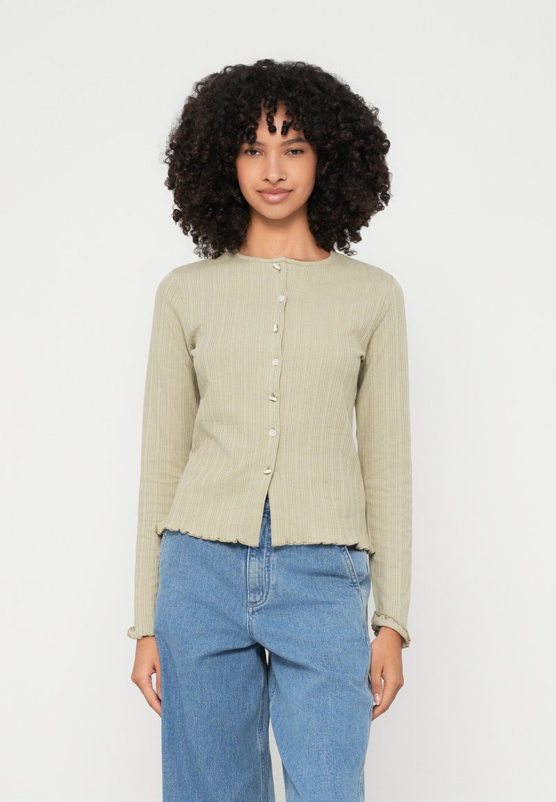 Μακρυμάνικο, ριμπ πλεκτό κασκόλ σε ανοιχτό πράσινο χρώμα με στρογγυλή λαιμόκοψη και μικρά κουμπιά. Διαθέτει διακοσμητική ραφή στο τελείωμα και εφαρμοστή σιλουέτα.