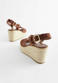 Sandali con zeppa in suede marrone, con fibbia e design a fantasia. Dettaglio in juta intrecciata sulla suola, con accenti dorati e superficie testurizzata.