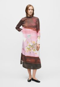 Permatomas, ilgomis rankovėmis suknelė su abstrakčiais rožinės ir rudos spalvų raštais, apimanti gėlių motyvus ir aukštą kaklo liniją, siekianti pusiau blauzdos ilgį.