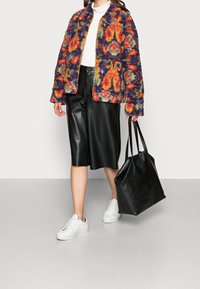 Multicolore textuurjack met bloemdesign, gecombineerd met een zwarte leren rok, witte sneakers en een zwarte tote bag. Gladde oppervlakten en gevarieerde kleuren.