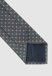 Mintázott nyakkendő, geometrikus designnal kékkel és fehérrel egy sötét háttéren. Texturált anyag, egységes tengerészkék alsó résszel.