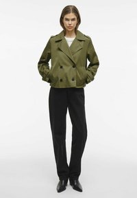 Olīvu zaļa divrindu žakete ar divām melnām pogām, ar apkakli un sānu kabatām, kopā ar melnām augstas jostas biksēm.