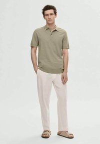 Ανοιχτό πράσινο πόλο μπλουζάκι με ριχτό γιακά και κοντά μανίκια, συνδυασμένο με κρεμ παντελόνι και καφέ σαγιονάρες. Απλός σχεδιασμός.