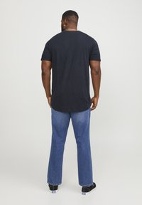 Camiseta negra de manga corta con dobladillo redondeado, combinada con jeans rectos de color azul claro y zapatos negros. Un atuendo simple y casual.