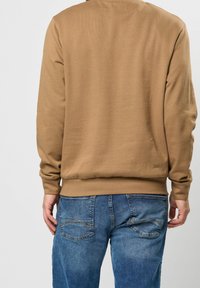 Sudadera marrón de canalé con mangas largas, que presenta un cuello redondo y puños elásticos, combinada con jeans de mezclilla azules con bolsillos traseros visibles.