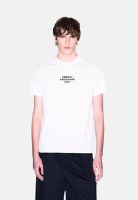 Biela bavlnená tričko s čiernym potlačeným logom "ARMANI EXCHANGE 1991" umiestneným v strede na hrudi. Kolo krk, krátke rukávy, voľný strih.