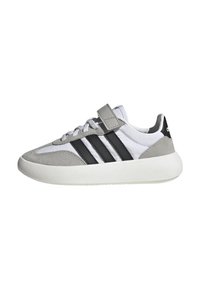 Scarpe sportive grigie e bianche con dettagli in suede, strisce nere e una cintura a strappo. Punta arrotondata e suola in gomma per il supporto.