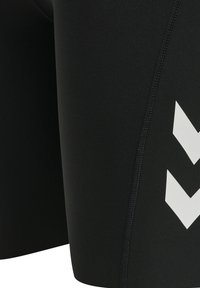 Svarta atletiska shorts i elastiskt material, med en vit chevron-logotyp och kontrasterande sömmar längs sidorna.